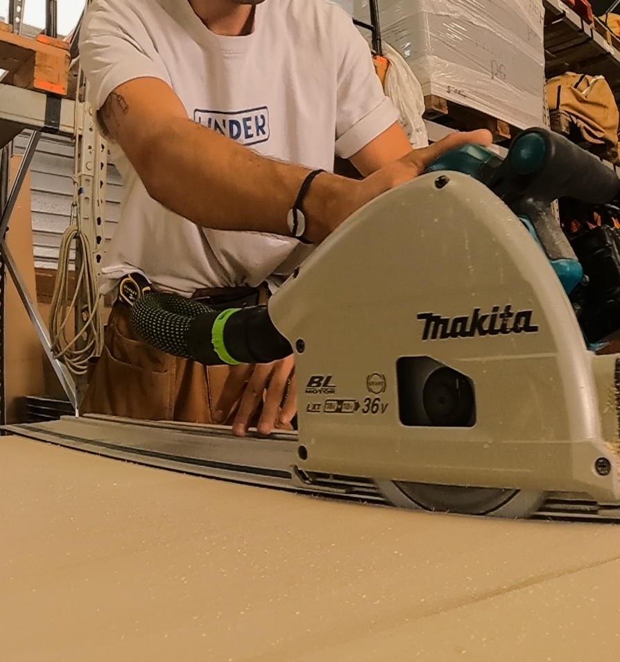 Un homme découpe un panneau de contreplaqué à l'aide d'une scie plongeante de la marque Makita.