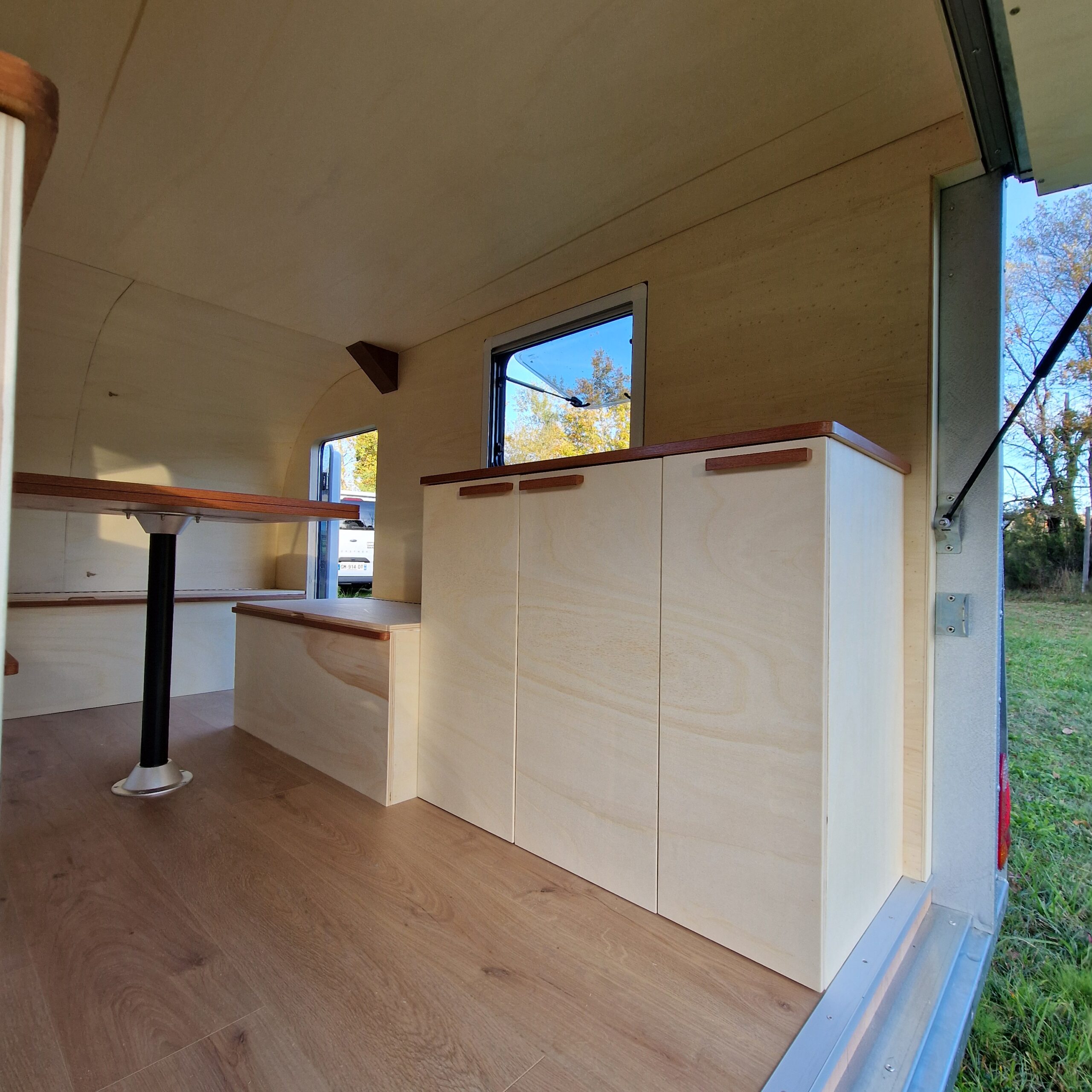 Aménagement intérieur côté droit d'une remorque à Bordeaux avec baie ouvrante, habillage mural en bois et banquette coffre.