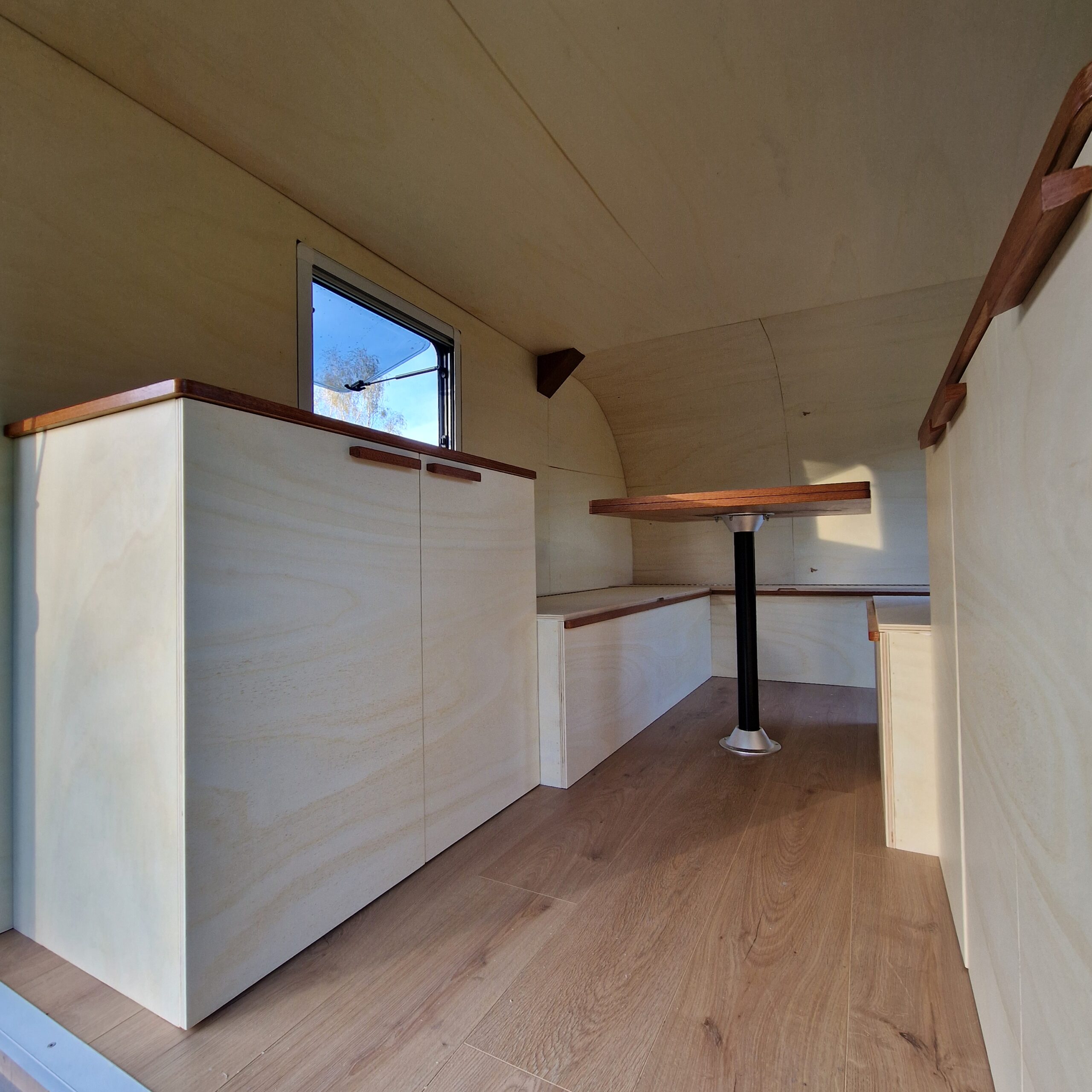 Vue de l'aménagement intérieur d'une remorque avec banquette en U, table escamotable, baie ouvrante et meubles de rangement à Bordeaux.