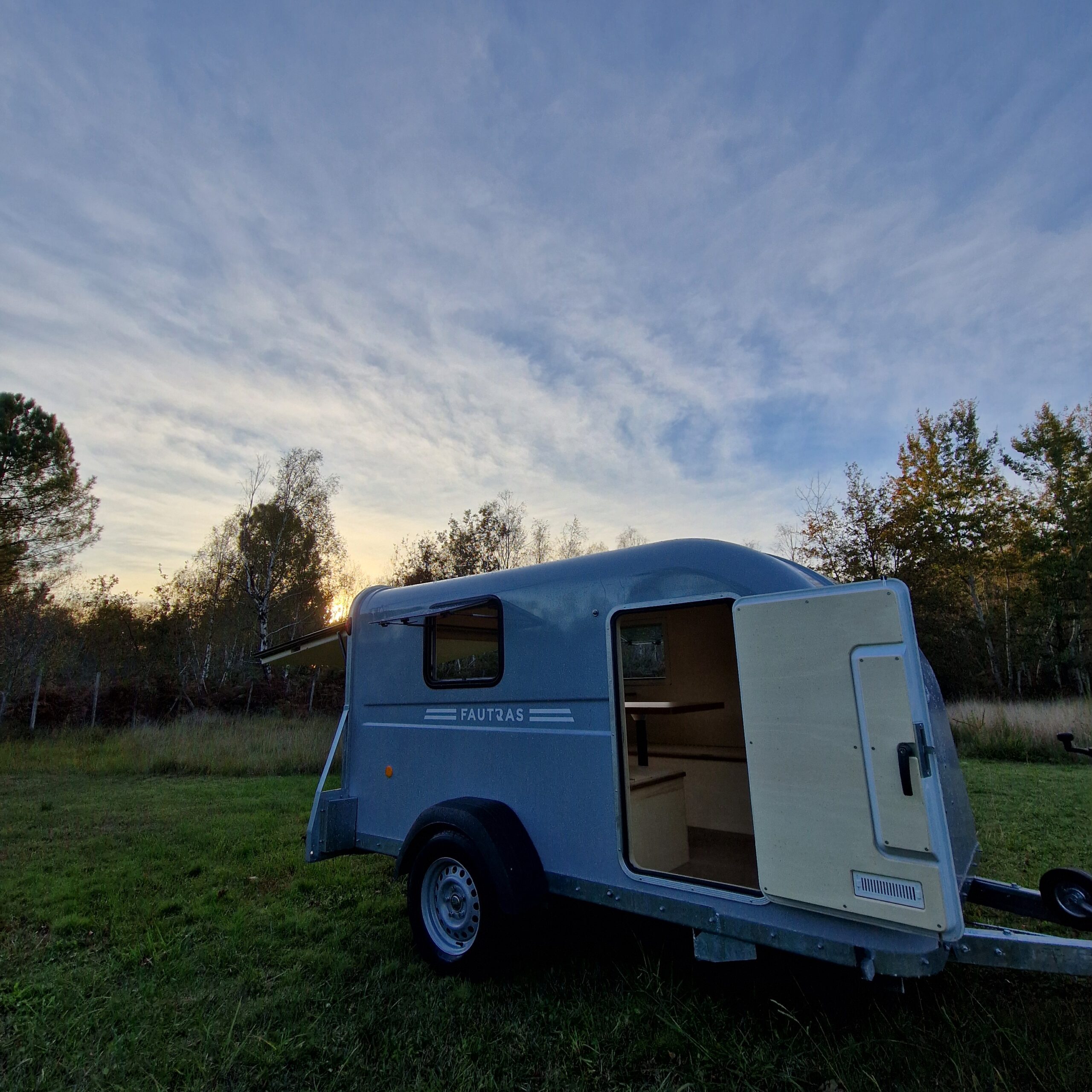 Vue latérale extérieure d'une remorque aménagée à Bordeaux présentant une baie ouvrante, une porte habillée de bois et une grille d'aération basse.