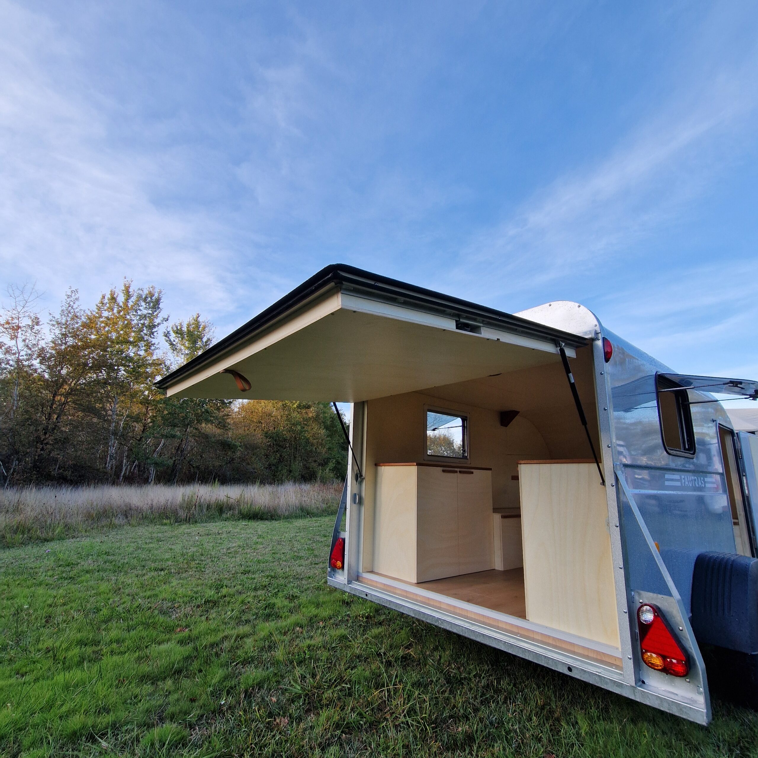 Vue arrière d'une remorque aménagée avec habillage du hayon en bois vernis, meubles latéraux sur mesure et parquet stratifié à Bordeaux.