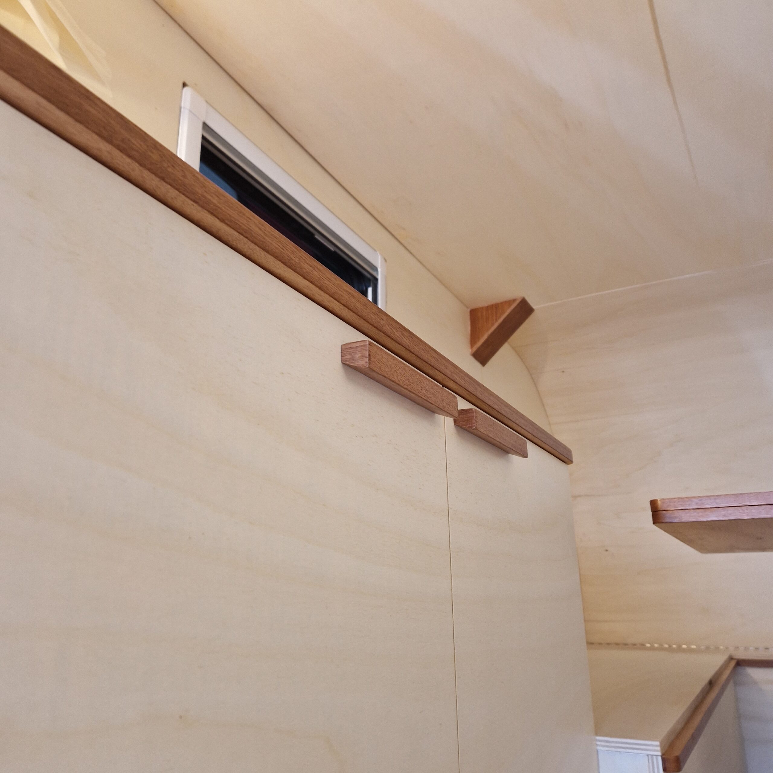 Zoom sur des poignées en bois exotique faites main pour un meuble de rangement sur mesure dans une remorque aménagée à Bordeaux.